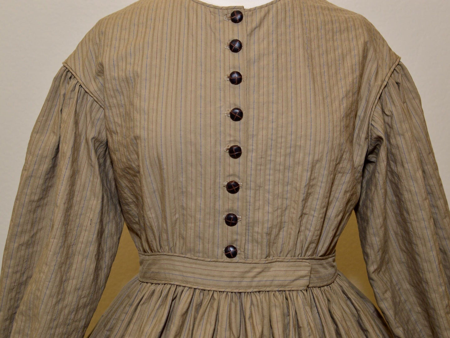A photo of the bodice of a brown 1860s dress shows the piping on the neck, armscyes, and waistband