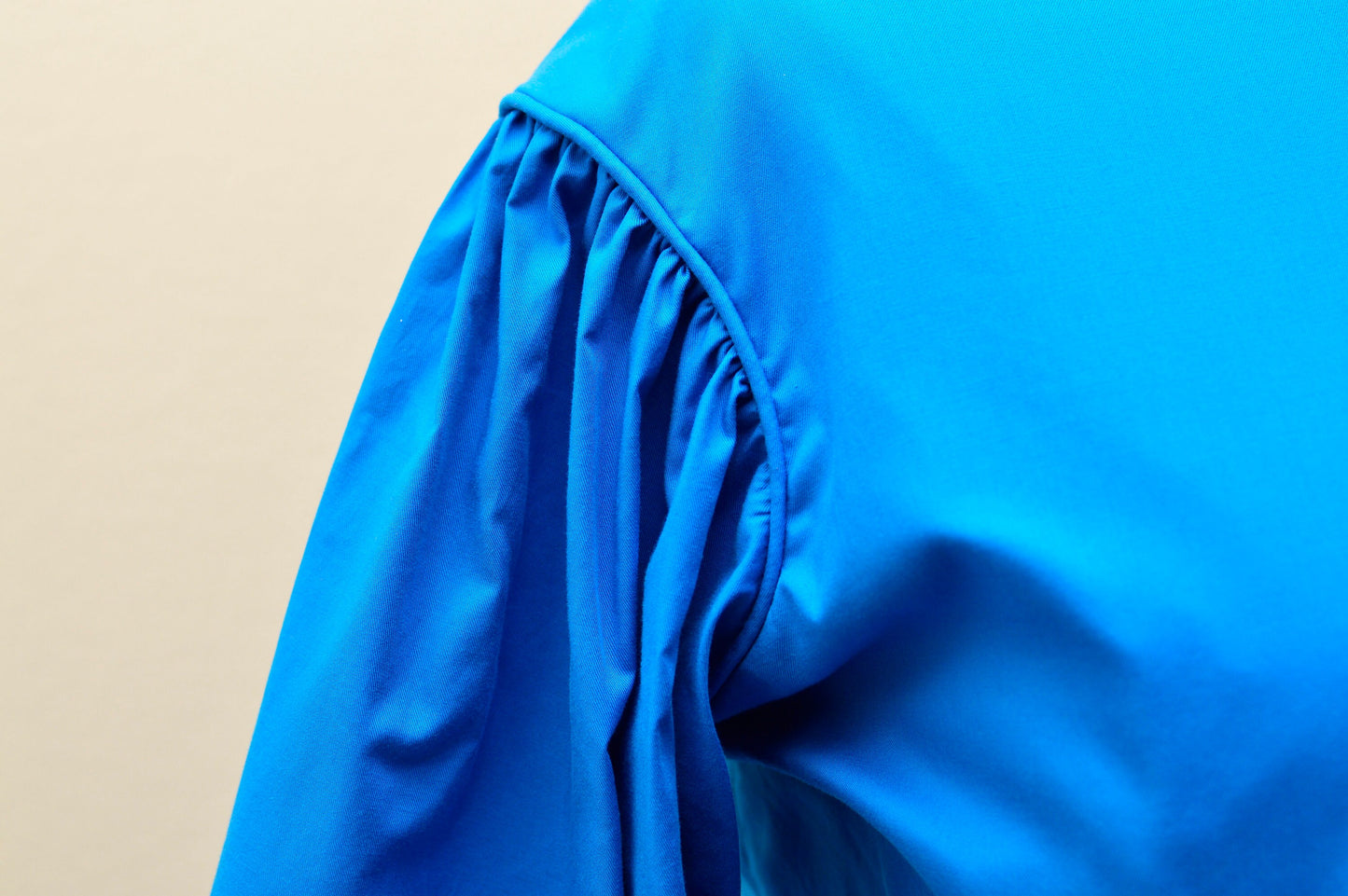 A close-up photos shows the piping on the armscye of a blue 1860s dress