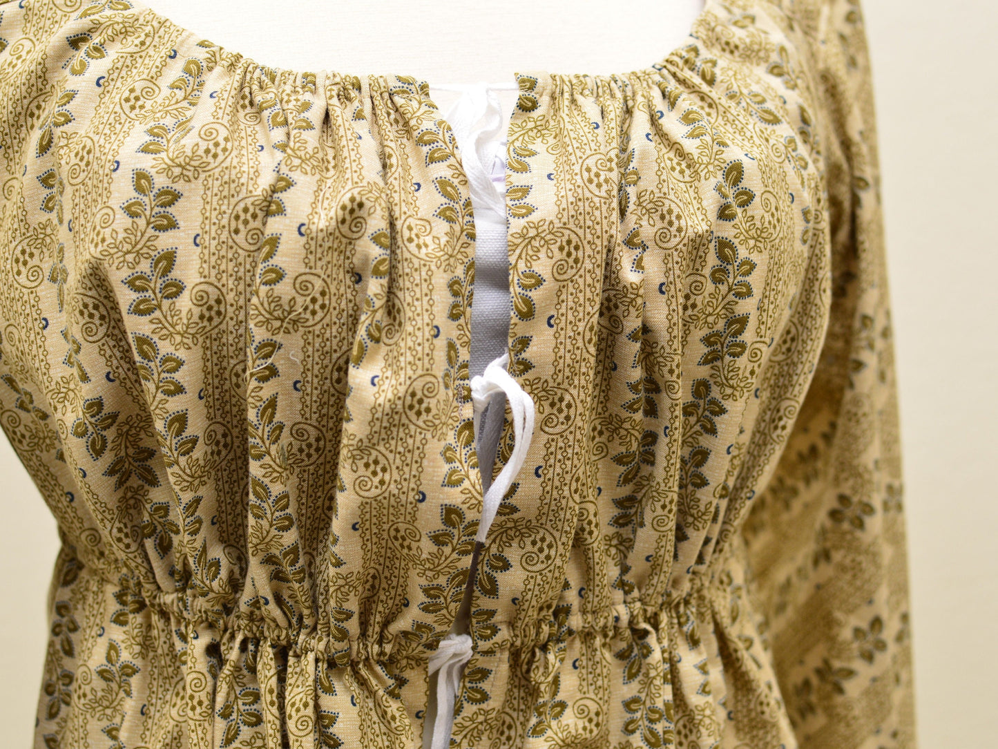 A close-up shows the front closure on a tan floral Regency gown: three ties made of cotton twill tape.