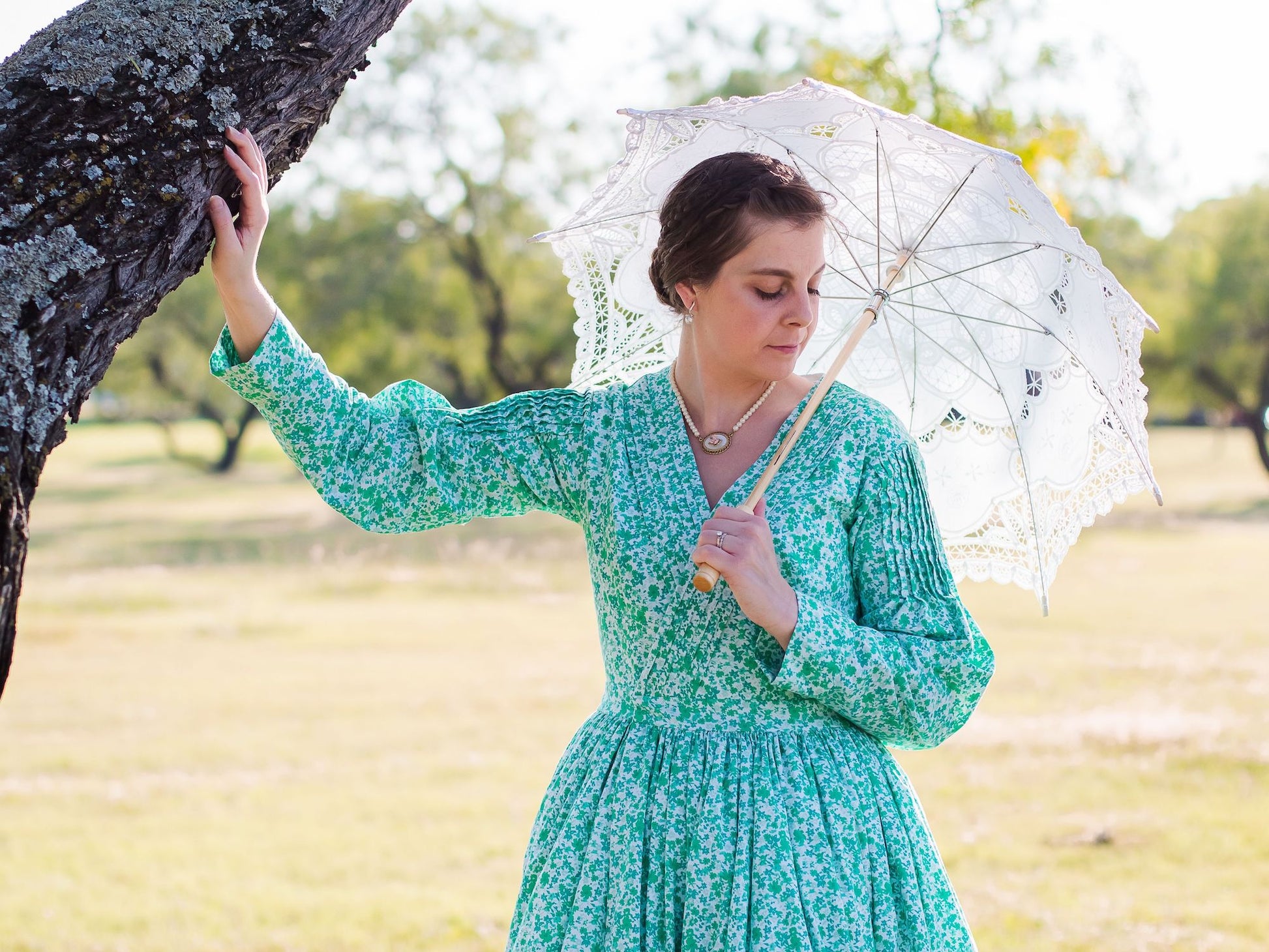 A model wears a mid-Victorian dress while holding a white lace umbrella