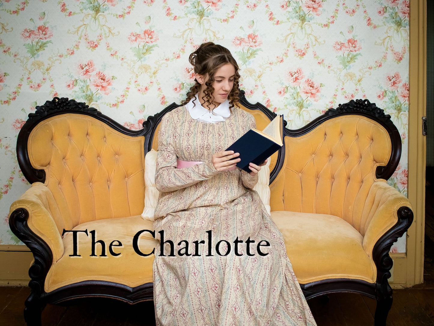 A girl wears Regency attire while sitting on an antique couch and reading