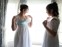 Load image into Gallery viewer, Two girls stand by a bay window while getting dressed in Regency undergarments
