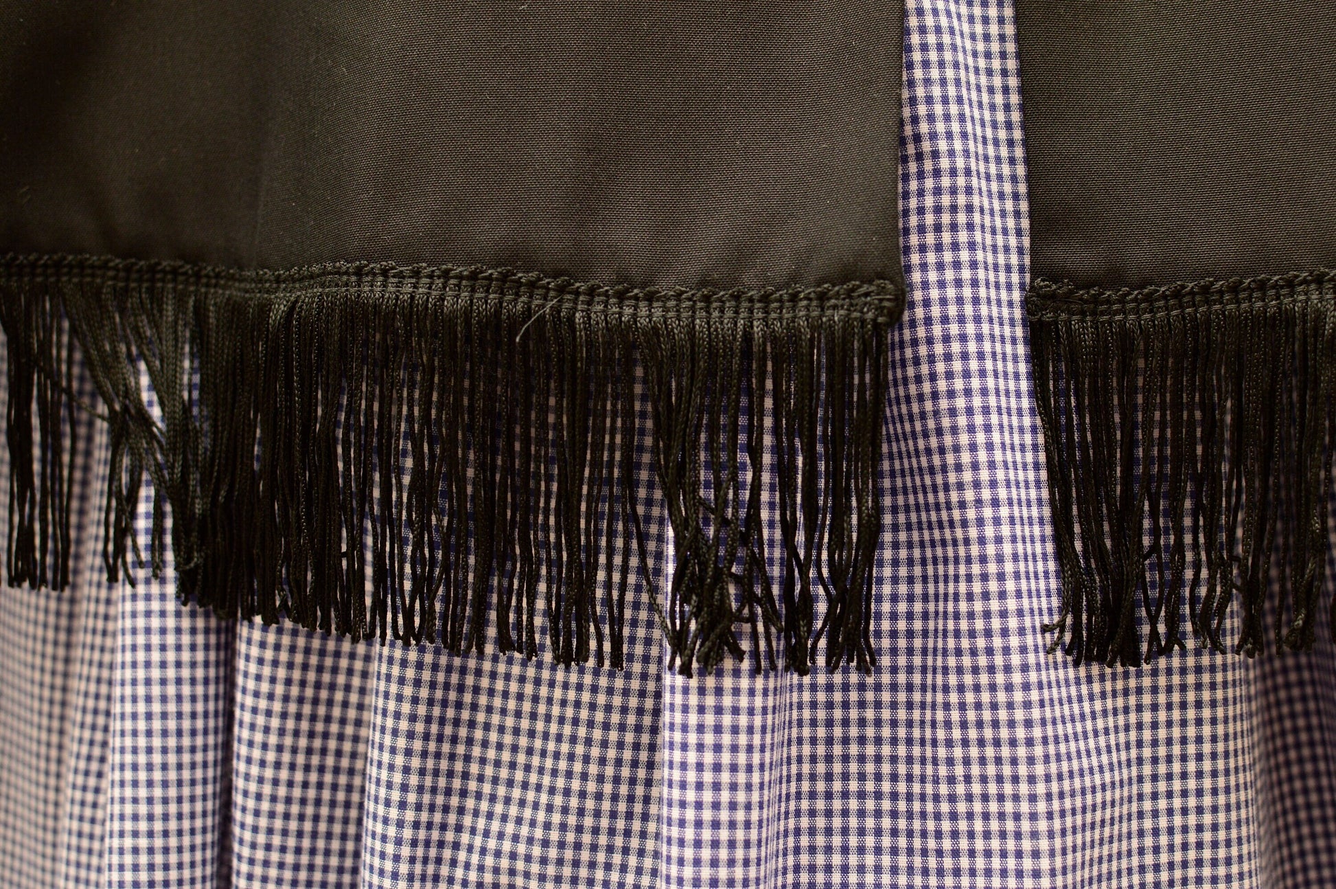 A close-up shows a wide fringe around the bottom edge of a black wool cape